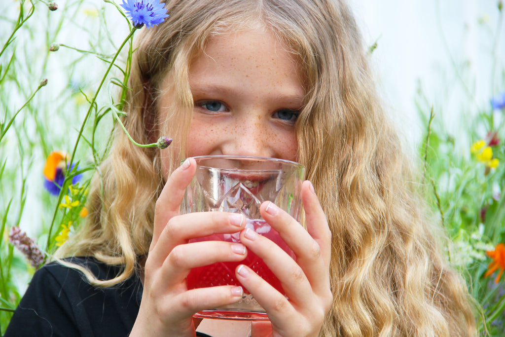 Green Vitality meisje drnkt EM drink buiten in veld met bloemen